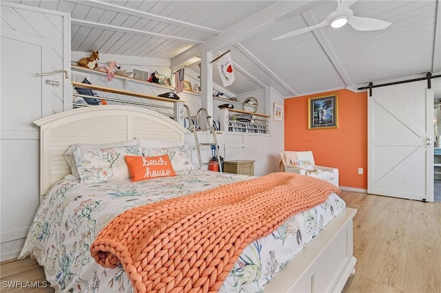 bedroom with lofted ceiling with beams, a barn door, wood finished floors, a ceiling fan, and baseboards