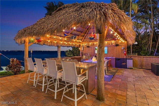 view of patio / terrace featuring outdoor dry bar, a gazebo, a water view, and fence