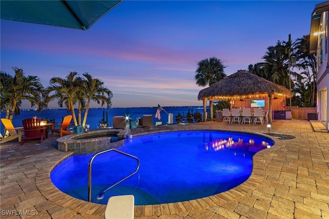 pool at dusk with an outdoor fire pit, a pool with connected hot tub, outdoor dry bar, a gazebo, and a patio area