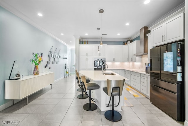 kitchen featuring white cabinetry, stainless steel fridge, hanging light fixtures, a center island with sink, and wall chimney exhaust hood