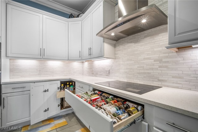 kitchen with tasteful backsplash, white cabinetry, black electric stovetop, light stone counters, and wall chimney exhaust hood