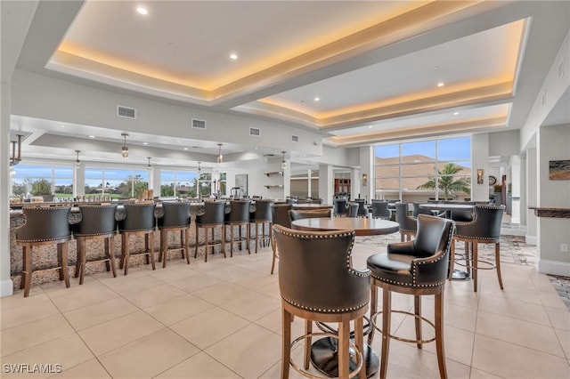 dining space with a healthy amount of sunlight, a tray ceiling, and light tile patterned floors