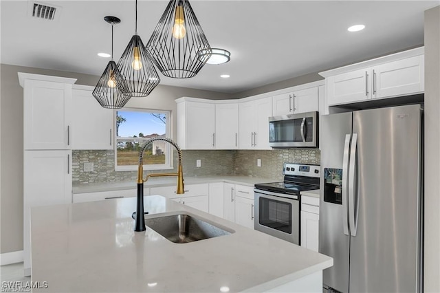 kitchen with sink, appliances with stainless steel finishes, hanging light fixtures, white cabinets, and a kitchen island