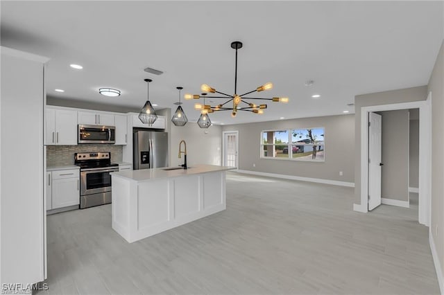 kitchen featuring decorative light fixtures, an island with sink, white cabinets, backsplash, and stainless steel appliances