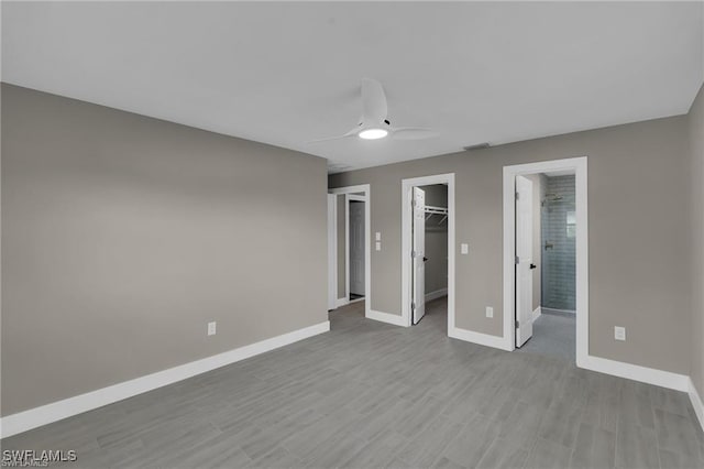 unfurnished bedroom with ensuite bathroom, a walk in closet, a closet, ceiling fan, and light hardwood / wood-style floors