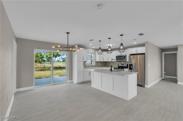 kitchen with a kitchen island with sink, stainless steel appliances, decorative backsplash, white cabinets, and decorative light fixtures