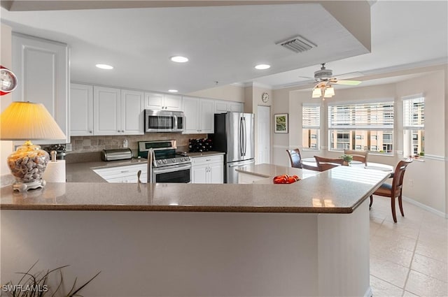 kitchen featuring light tile patterned floors, appliances with stainless steel finishes, backsplash, white cabinets, and kitchen peninsula