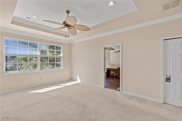 unfurnished bedroom featuring ensuite bathroom, light colored carpet, ceiling fan, a tray ceiling, and crown molding