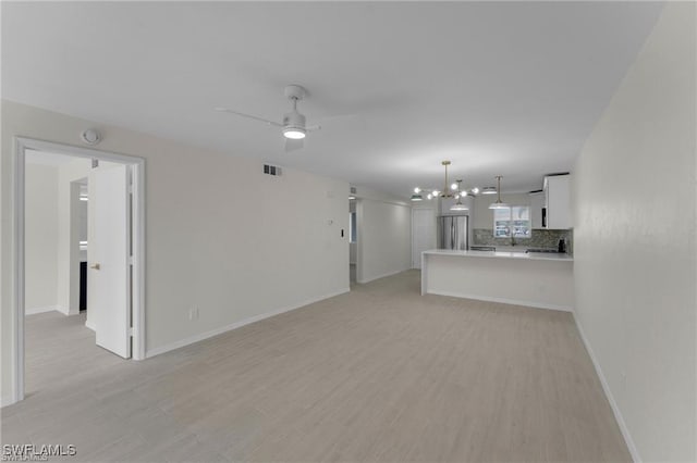 unfurnished living room with ceiling fan with notable chandelier and light hardwood / wood-style floors