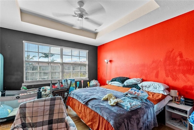 bedroom with a raised ceiling, hardwood / wood-style flooring, and ceiling fan