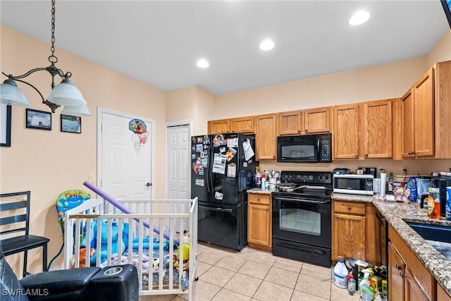 kitchen with pendant lighting, sink, light tile patterned floors, black appliances, and light stone countertops