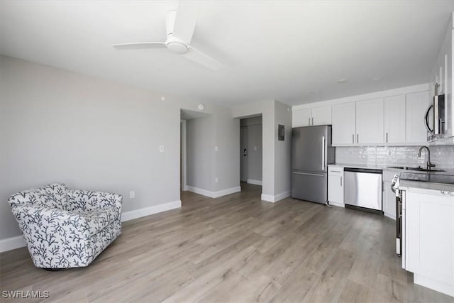 kitchen with appliances with stainless steel finishes, tasteful backsplash, white cabinetry, ceiling fan, and light wood-type flooring