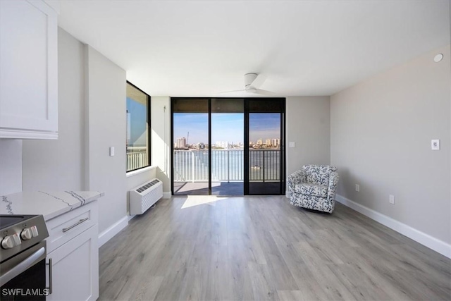 unfurnished room featuring light hardwood / wood-style flooring, a wall mounted AC, ceiling fan, and a wall of windows