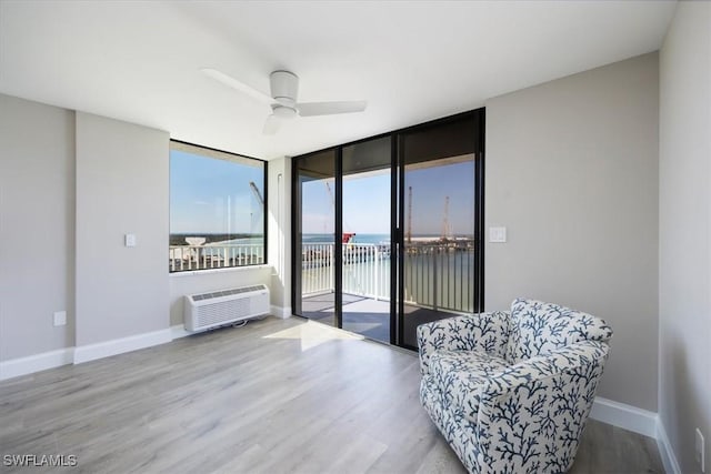 sitting room featuring a wall mounted AC, a water view, hardwood / wood-style floors, and ceiling fan