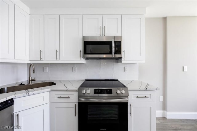 kitchen featuring stainless steel appliances, white cabinets, light stone counters, and decorative backsplash