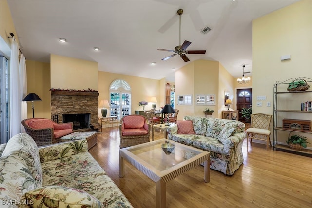 living room featuring high vaulted ceiling, a stone fireplace, ceiling fan with notable chandelier, and light hardwood / wood-style floors