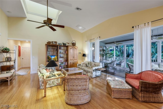 living room with high vaulted ceiling, a skylight, light hardwood / wood-style floors, and ceiling fan