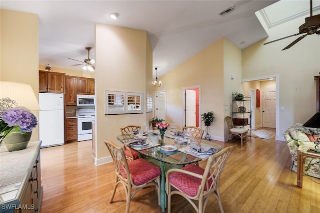 dining space featuring high vaulted ceiling, ceiling fan with notable chandelier, light wood-type flooring, and a skylight