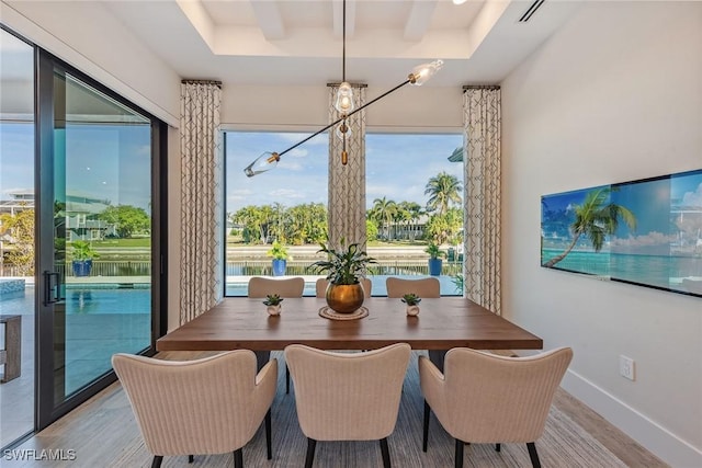 dining space with a raised ceiling, a chandelier, and light wood-type flooring