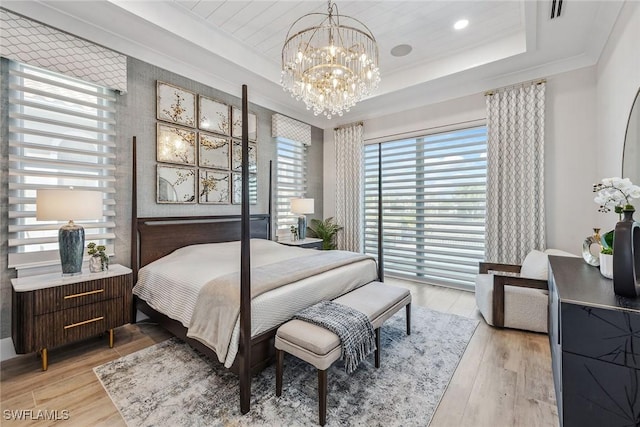 bedroom with a raised ceiling, crown molding, a notable chandelier, and light hardwood / wood-style floors