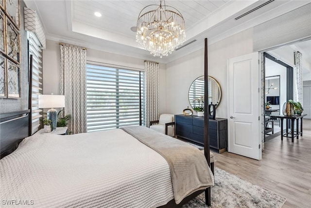 bedroom featuring ornamental molding, a tray ceiling, a chandelier, and light hardwood / wood-style floors