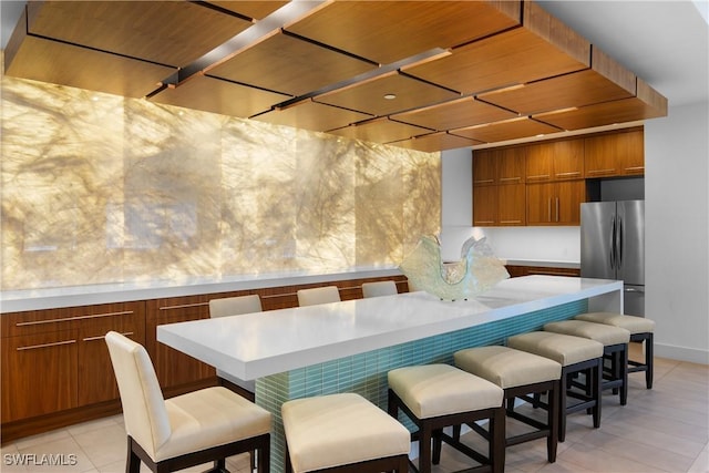 kitchen with light tile patterned flooring, stainless steel fridge, and a breakfast bar area