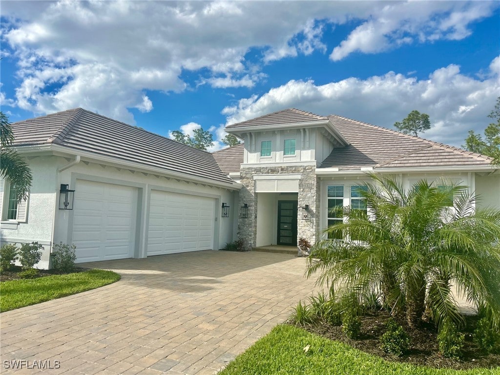 view of front of property with a tiled roof, decorative driveway, an attached garage, and stucco siding