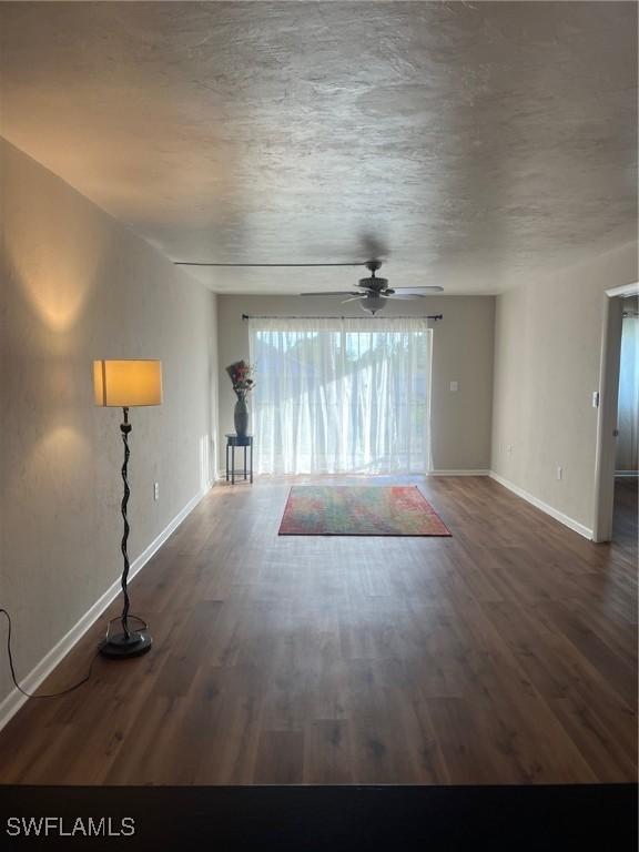 unfurnished living room featuring ceiling fan, dark wood-type flooring, and a textured ceiling