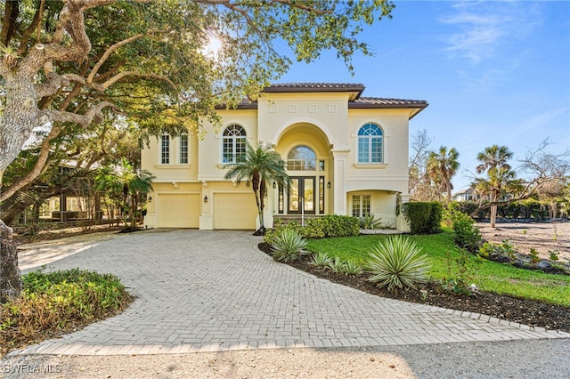 mediterranean / spanish-style home with a garage, a tiled roof, decorative driveway, french doors, and stucco siding