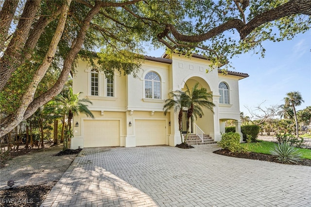 mediterranean / spanish-style house with a garage, decorative driveway, a tile roof, and stucco siding