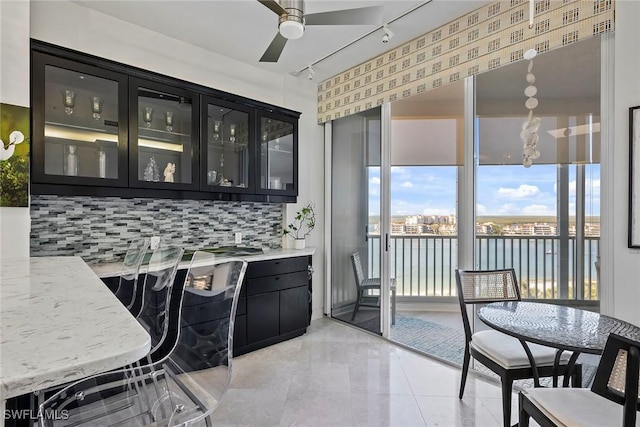 kitchen featuring a water view, ceiling fan, light stone counters, and tasteful backsplash