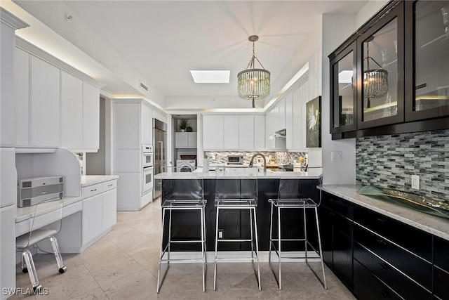 kitchen featuring white cabinetry, tasteful backsplash, a kitchen bar, decorative light fixtures, and kitchen peninsula