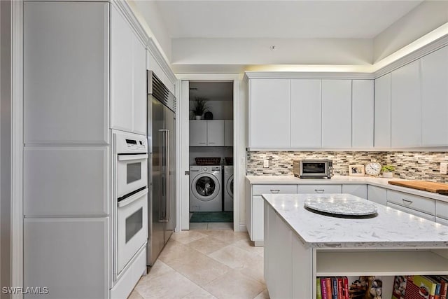 kitchen with light stone countertops, independent washer and dryer, and white cabinets