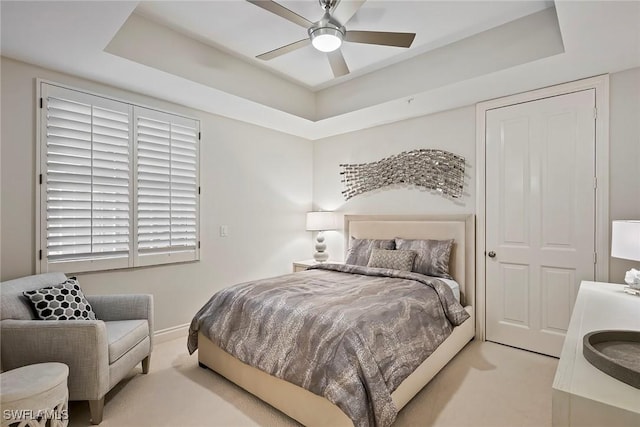 bedroom with ceiling fan, light colored carpet, and a raised ceiling