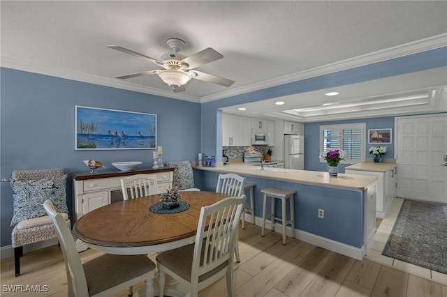 dining space with baseboards, light wood-style flooring, ceiling fan, ornamental molding, and a tray ceiling