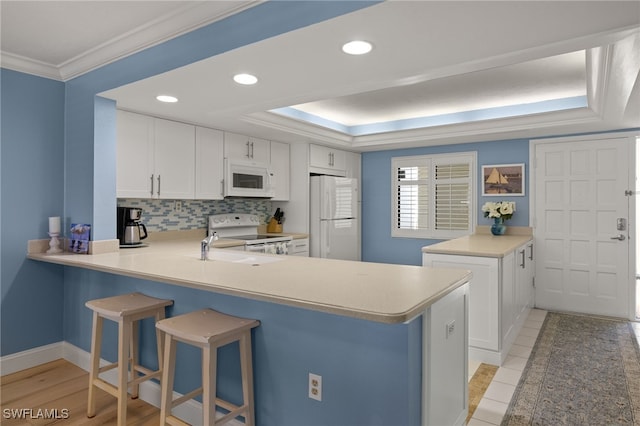 kitchen featuring white appliances, kitchen peninsula, and white cabinets