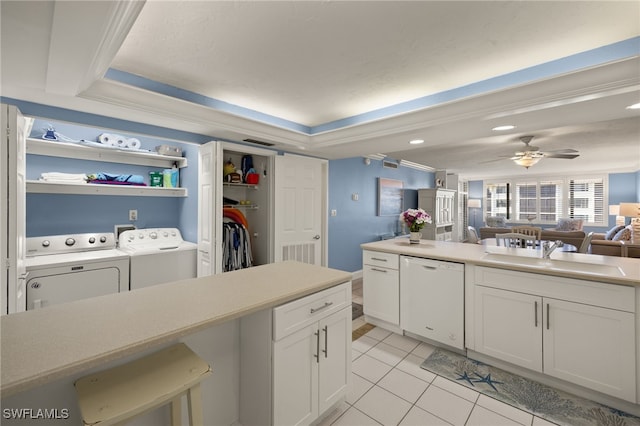 kitchen with independent washer and dryer, white dishwasher, light countertops, white cabinetry, and a sink