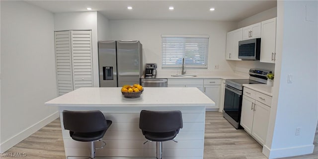 kitchen featuring a breakfast bar, stainless steel appliances, white cabinets, a kitchen island, and light wood-type flooring