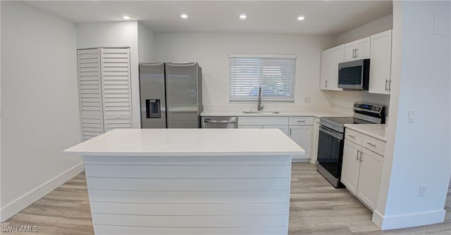 kitchen with sink, a center island, stainless steel appliances, light hardwood / wood-style floors, and white cabinets