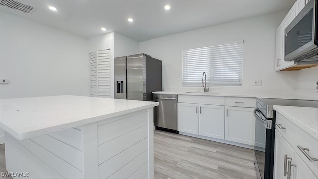 kitchen with sink, appliances with stainless steel finishes, light hardwood / wood-style floors, white cabinets, and a kitchen island