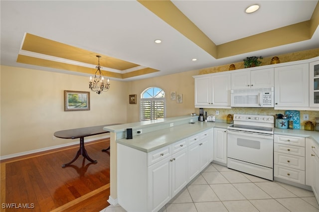 kitchen with kitchen peninsula, decorative light fixtures, white cabinetry, a tray ceiling, and white appliances