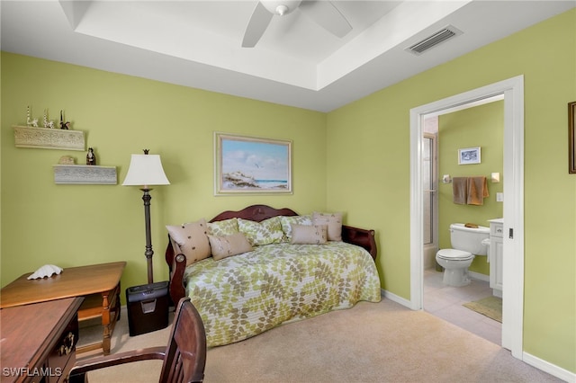 carpeted bedroom featuring ceiling fan, ensuite bath, and a tray ceiling