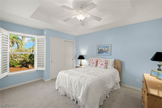 carpeted bedroom with a tray ceiling, a closet, and ceiling fan