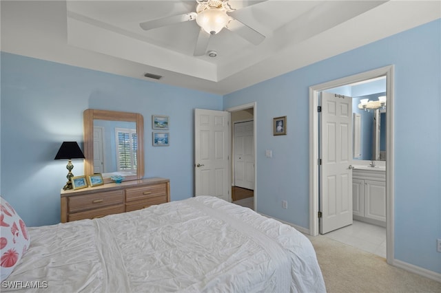 bedroom featuring a raised ceiling, connected bathroom, light colored carpet, and ceiling fan