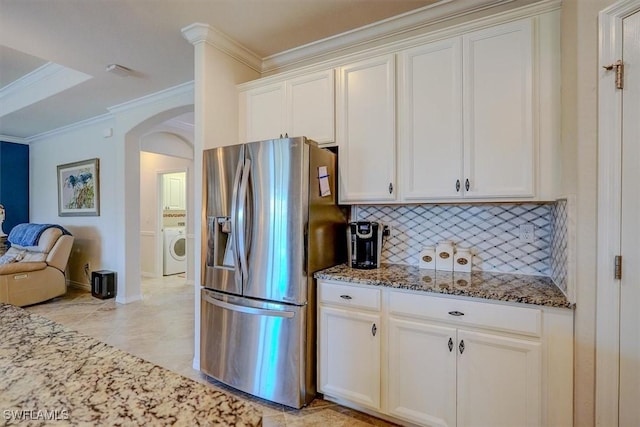 kitchen with crown molding, stainless steel fridge, washer / clothes dryer, decorative backsplash, and dark stone counters