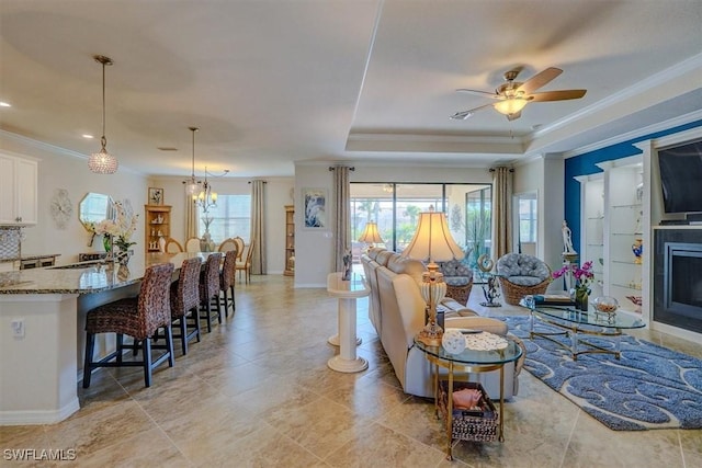 living room featuring crown molding, a raised ceiling, and ceiling fan with notable chandelier