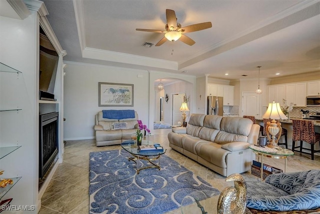 tiled living room featuring crown molding, a fireplace, and a tray ceiling