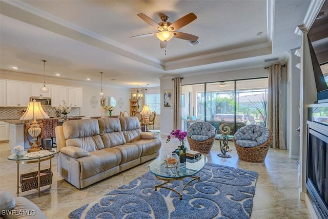 living room featuring a raised ceiling, crown molding, and ceiling fan with notable chandelier