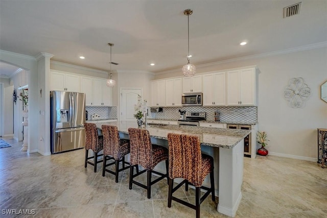 kitchen with appliances with stainless steel finishes, a breakfast bar, an island with sink, white cabinets, and light stone countertops