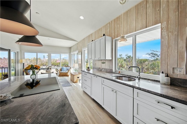 kitchen featuring pendant lighting, sink, lofted ceiling, white cabinetry, and dark stone countertops